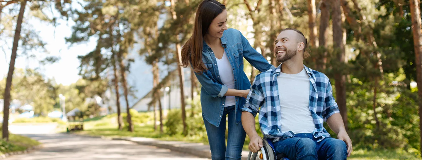 Federated Insurance | Disability Income Awareness Month | Lady pushing a man in a wheelchair on paved path; laughing and smiling at each other.