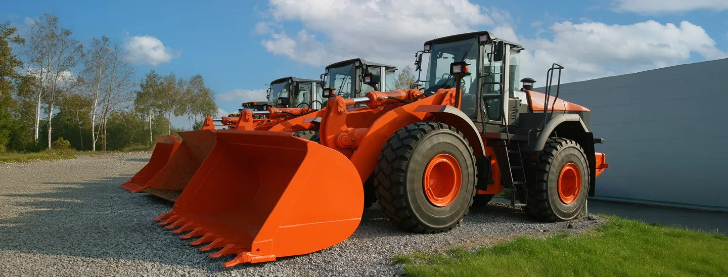 AED Associated Equipment Distributors | Federated Insurance | Orange tractors with bucket attachments lined up on a gravel surface