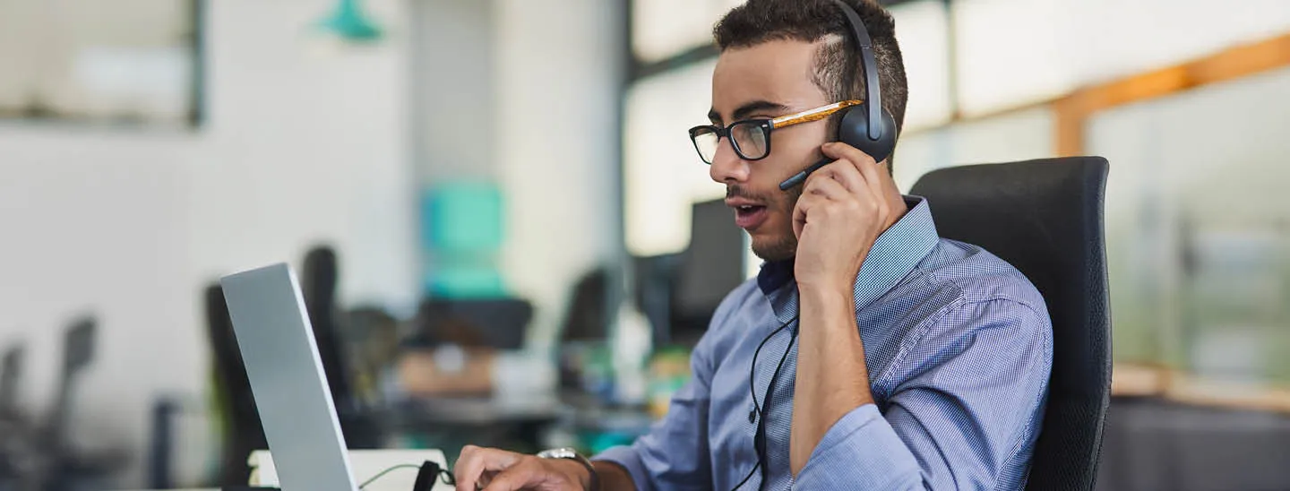 Professional working at a desk in a modern office environment, wearing a headset and using a laptop, symbolizing diverse career areas and workplace collaboration.