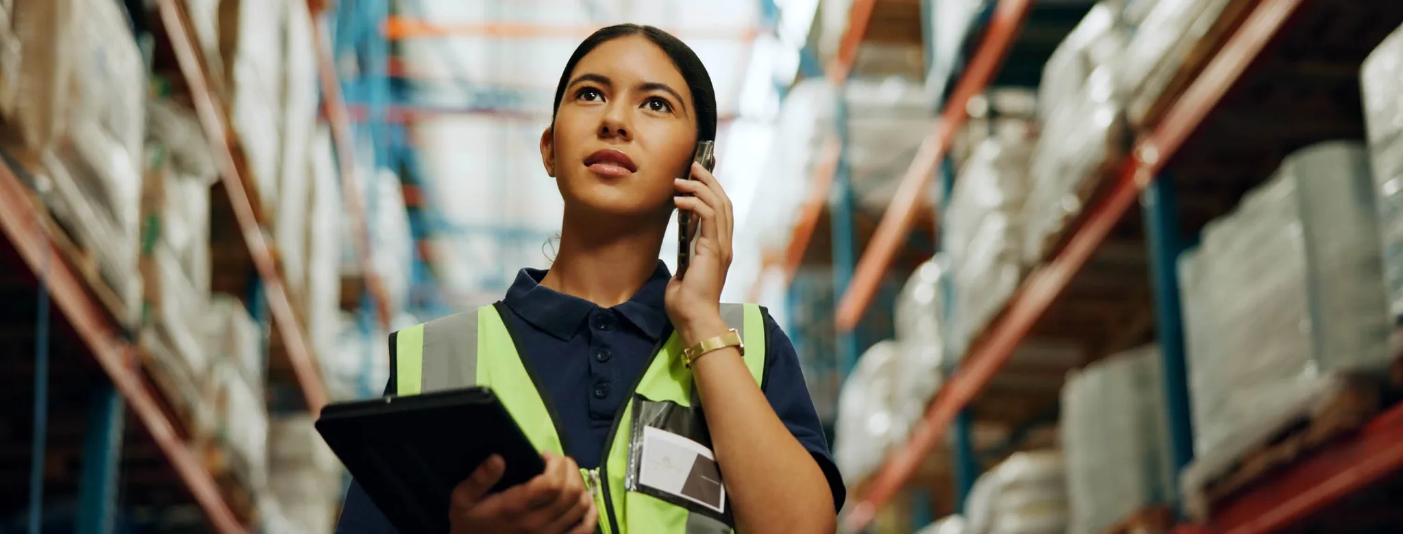 Woman speaking on cellphone wearing safety vest in warehouse