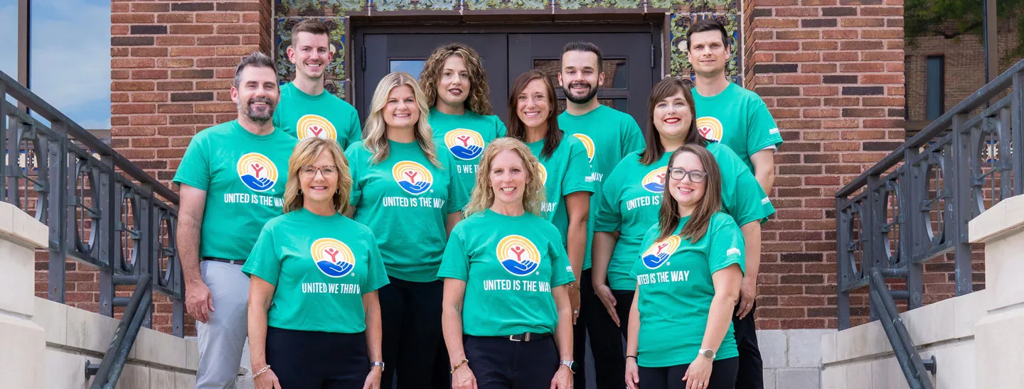 A group of Federated employees stands outside an office entrance wearing matching green United Way campaign shirts. The image highlights the organization's commitment to employee giving, volunteerism, community partnerships, and support for local United Way initiatives.
