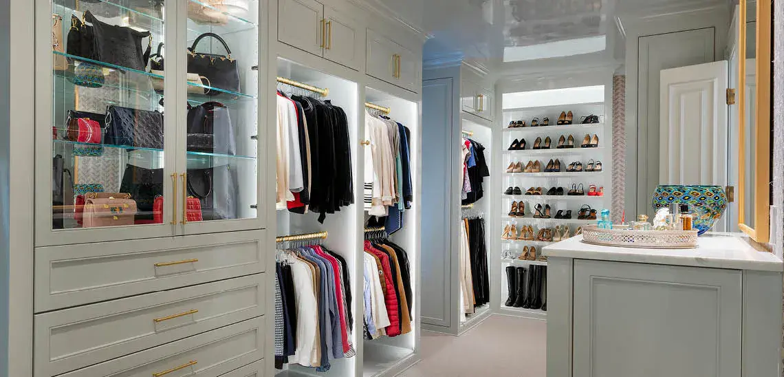 Elegant custom walk-in closet with glass-front cabinets, organized clothing racks, and shoe shelving designed by Association of Closet and Storage Professionals (ACSP).