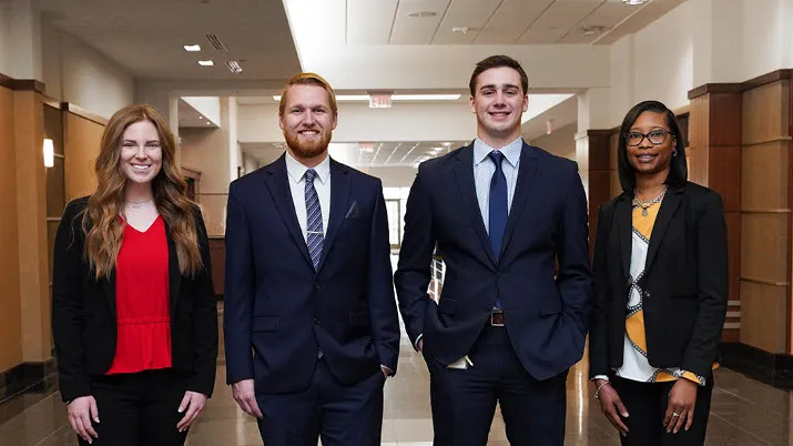 Group of professionals in formal business attire standing in a modern office hallway, representing the company’s hiring process and career opportunities.