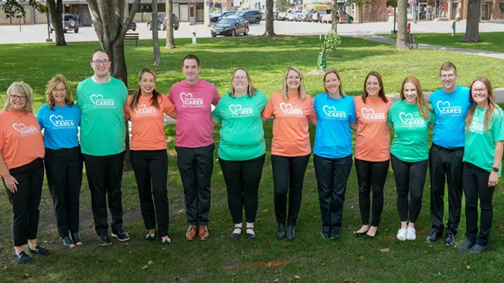 Employees wearing colorful company volunteer shirts standing together outdoors, representing community engagement and giving back culture.