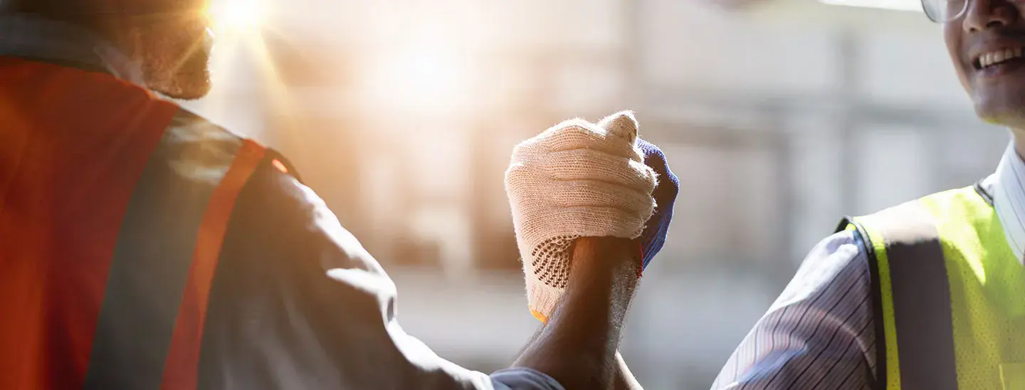Workers in yellow and orange vests lock hands in a handshake