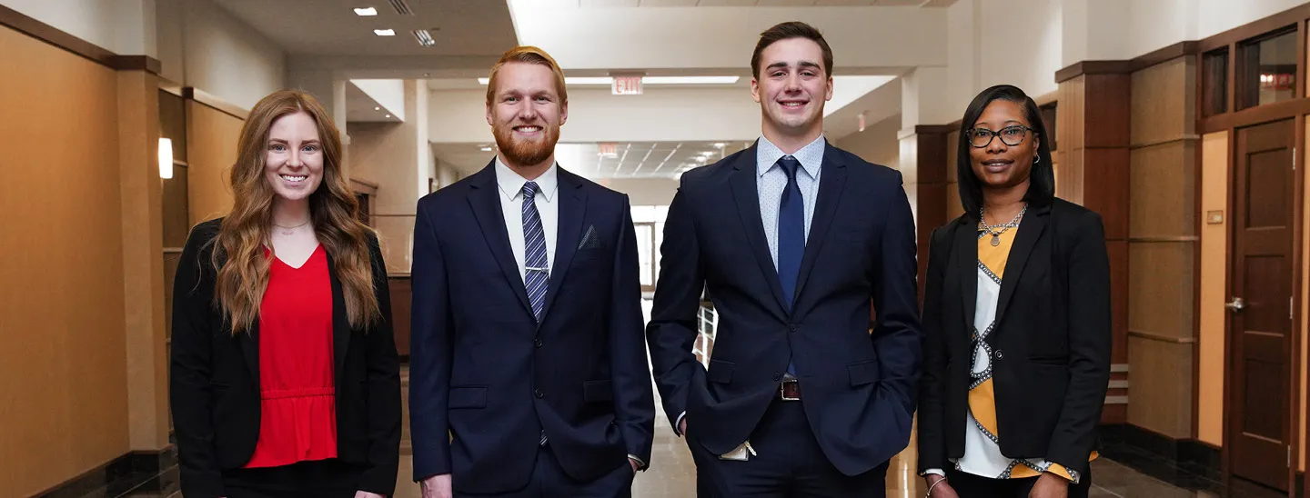 Four professionals in business attire standing in a modern office hallway with an overlay text reading ‘Join Our Team’ and a button to search job openings, representing career opportunities and the hiring process.