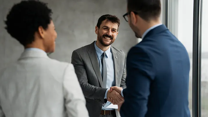 Business professionals in formal attire shaking hands in a modern office setting, symbolizing job opportunities and successful hiring.