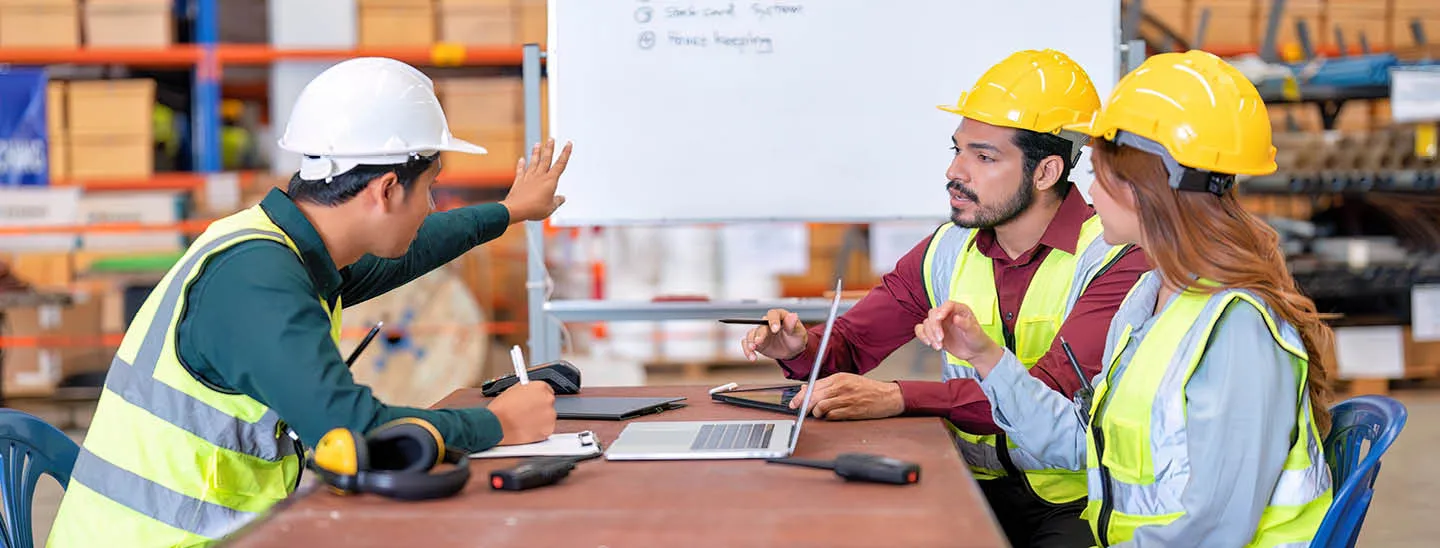 Group of warehouse workers wearing PPE discussing employee training at a table