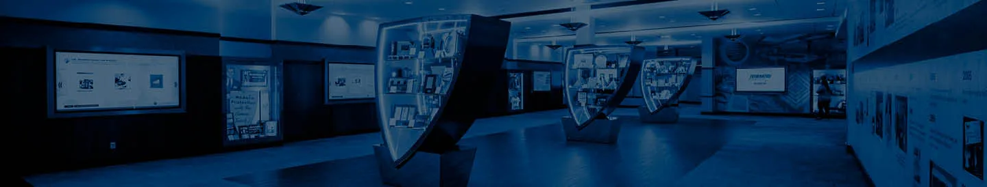 Modern corporate lobby with illuminated display cases shaped like shields, showcasing company history and achievements, surrounded by digital screens and informational panels.