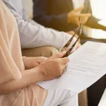 Adult reviewing business documents and eyeglasses during a meeting about business succession planning and insurance coverage options.